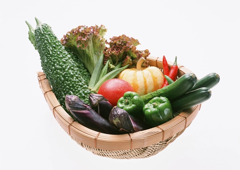 A woven basket filled with freshly harvested vegetables, including leafy greens, tomatoes, carrots and peppers