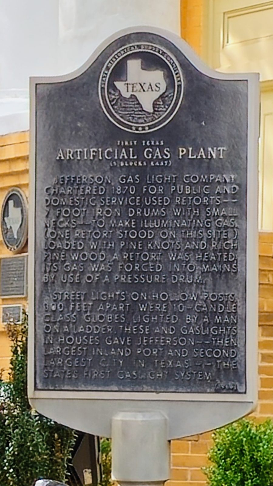 Weathered metal historical marker sign titled "Artificial Gas Plant" mounted on a post outdoors