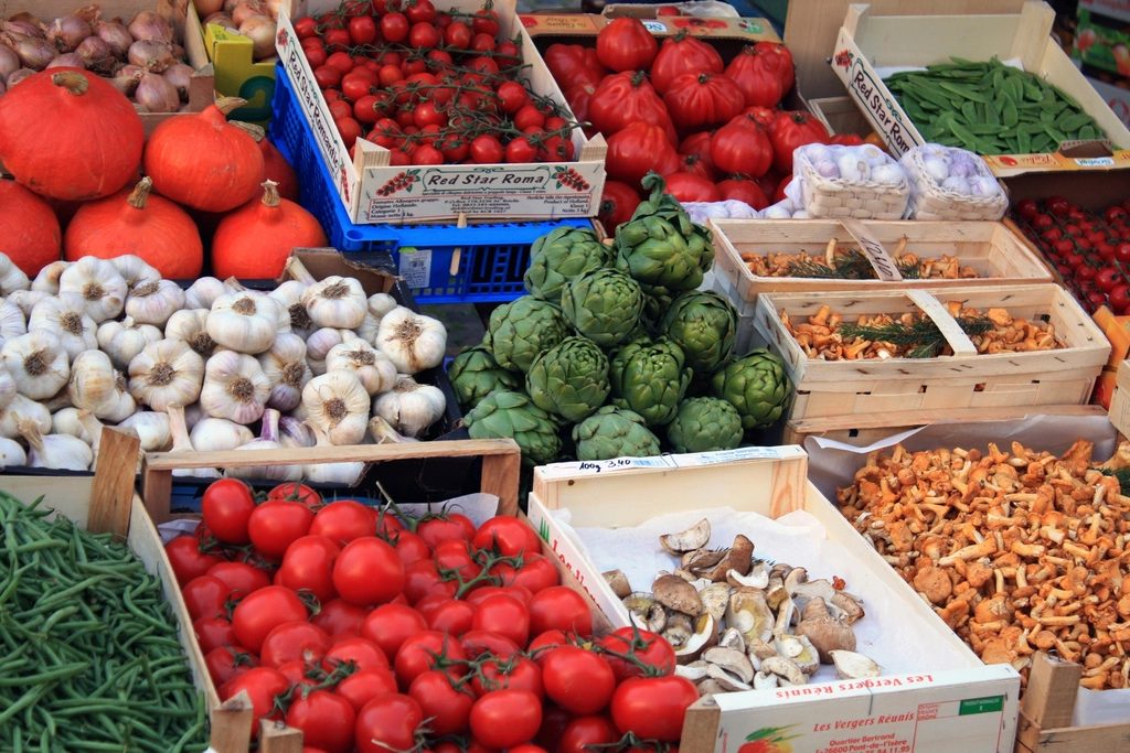 Wooden farm stand displaying crates of fresh vegetables including tomatoes, peppers, greens and root vegetables